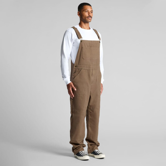 Canvas overalls in a brown shade, featuring adjustable straps and pockets, worn over a white long-sleeve top.