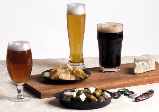 A craft beer glass set featuring three different beers: a dark stout, a pale lager, and an amber ale, alongside snacks.
