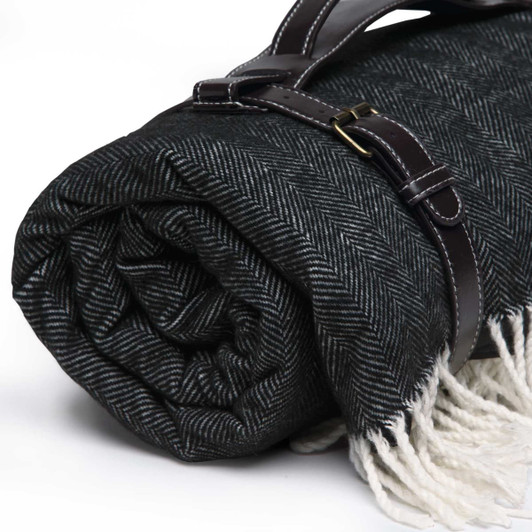 A rolled black and white herringbone picnic blanket secured with a brown strap, featuring fringe edges.