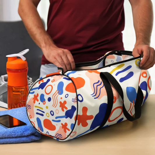 A colourful duffle bag with a vibrant abstract pattern, positioned next to a drink bottle and a towel on a table.