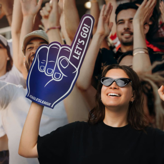 A foam hand supporter in blue and white, raised by a woman wearing sunglasses, amid an enthusiastic crowd.