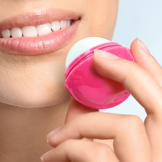 A pink lip balm ball is being applied to lips in close-up, featuring a round shape and smooth texture.