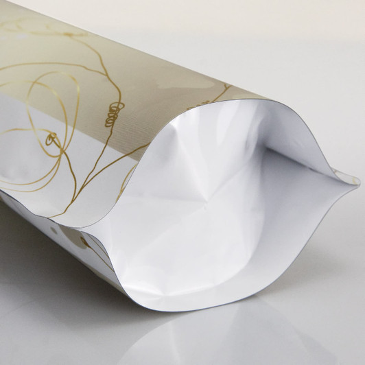 A small foil stand-up pouch in a gold and white design with a curved top, featuring a logo.