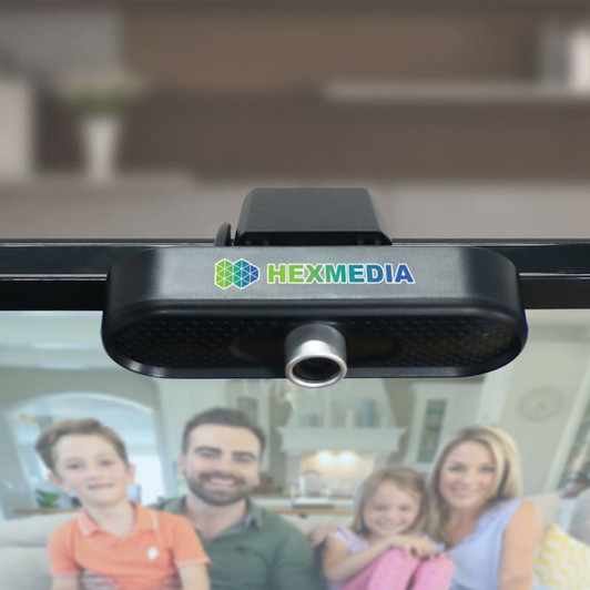 A black Helm Webcam Camera with a logo, mounted on a screen, overlooking a family in a home setting.