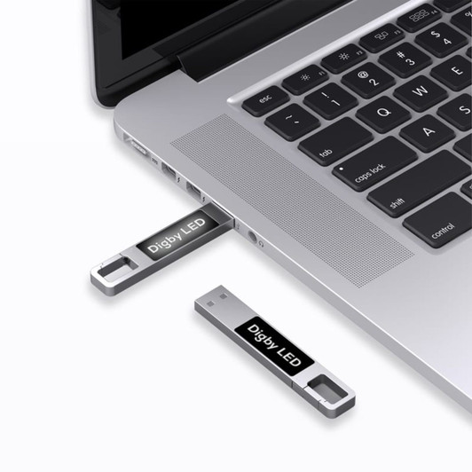 A silver LED flash drive connected to a laptop's USB port, featuring a logo on the drive.