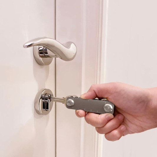 A silver multi-tool is being used to unlock a door, with a sleek door handle visible in the background.