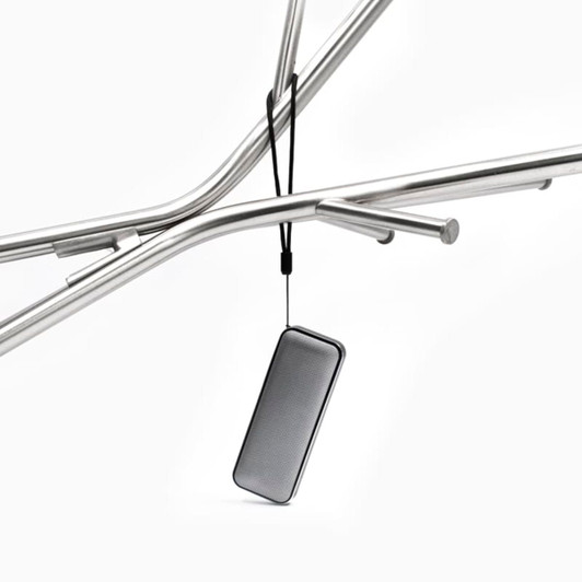 A compact black Bluetooth speaker hanging from a metal frame, featuring a sleek design and a strap.