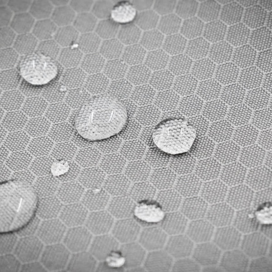 A close-up of a textured grey fabric with water droplets collecting on its honeycomb pattern, featuring a logo.