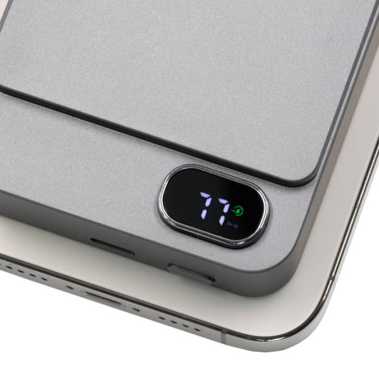 A grey magnetic wireless power bank with a digital battery indicator, resting on a phone.