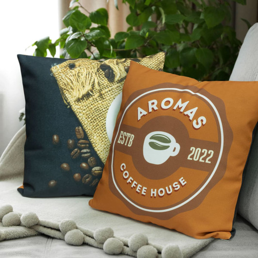 A pair of cushions featuring a coffee theme, with one side showcasing coffee beans and the other an orange design with a logo.