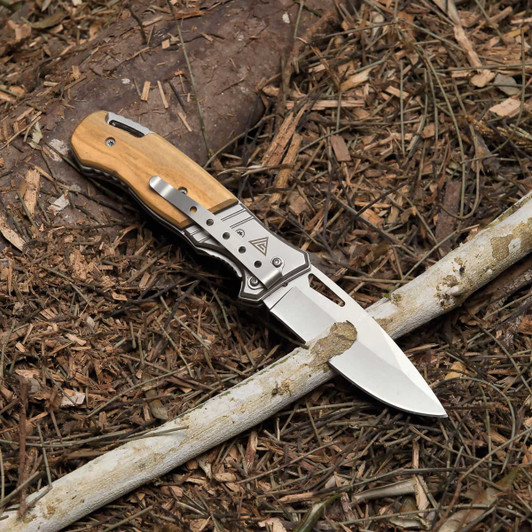 A pocket knife featuring a stainless steel blade and a wooden handle, resting on a bed of leaves and twigs.