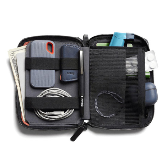 A compact, black toiletry bag containing a phone, cash, cables, a pen, and various small accessories. It features organisational straps.