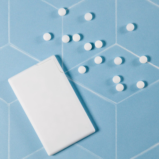 A white, rectangular container of sugar-free breath mints is next to scattered white mints on a blue background.