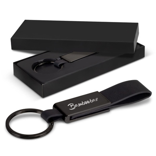 A black key ring with a leather strap and metal clip, displayed in a sleek black box.