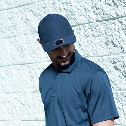 A man wearing a navy waffle fabric cap and polo shirt poses against a textured white wall. The cap features a logo.