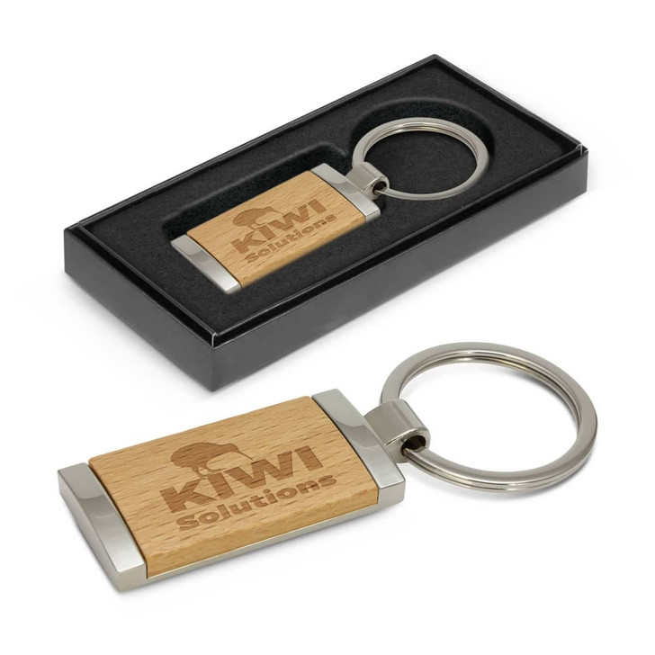 A wooden key ring with a silver metal clasp, presented in a black box. It features a logo on the wood.
