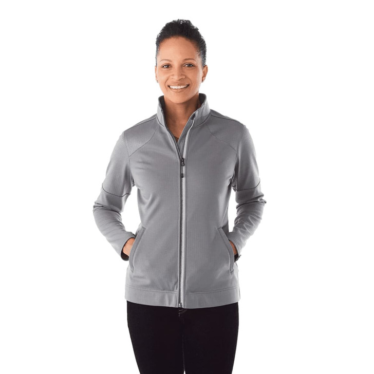 A woman is wearing a grey full zip performance jacket with thumb holes, featuring a sleek design and a logo.