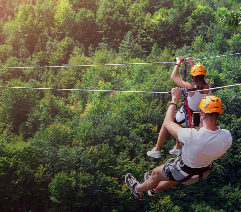 Man and woman on zip line hanging over forest.