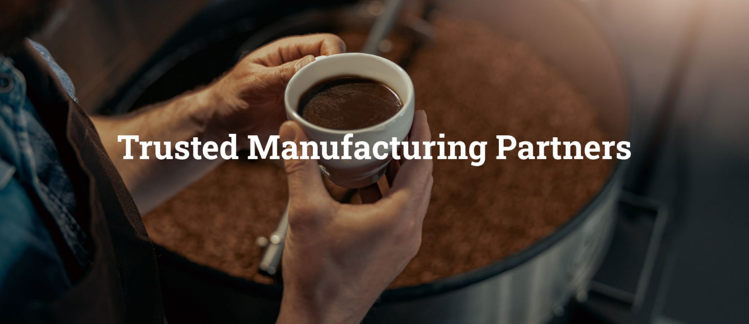 Person holding cup of coffee in front of industrial coffee machine.