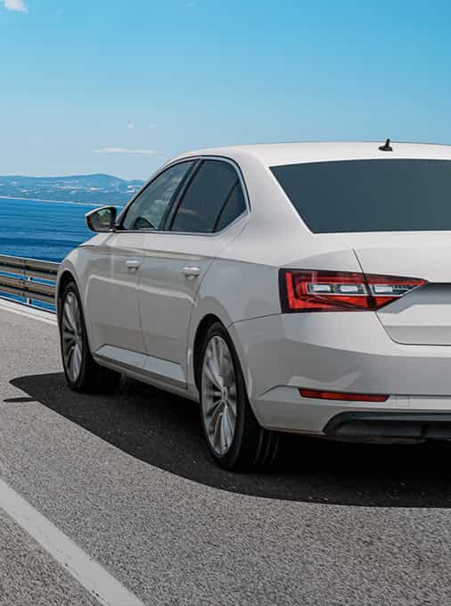 White car driving on road overlooking ocean.