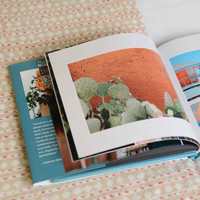 Open hardcover photo book with travel-themed layout showing cactus image on right page and layered printed pages beneath.