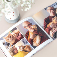 Open softcover photo book showing a collage of an elderly man holding an orange cat, styled beside a vase with small white flowers.