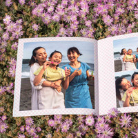 Softcover photo book open to beach family photos, placed on pink flowers background with patterned page design visible.
