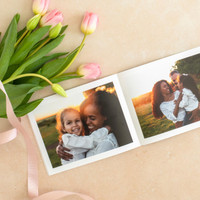 Open softcover photo book featuring mother and daughter portraits at sunset, styled with pink tulips and ribbon on neutral background.