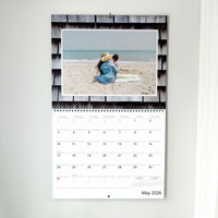 Spiral-bound wall calendar for May 2026 featuring a beach photo of a mother and child sitting on sand facing the ocean.