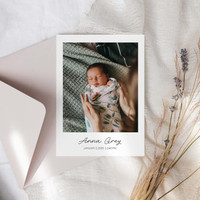 Folded birth announcement card with newborn portrait, baby name, and birth date text, styled with envelope and soft neutral decor.