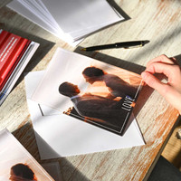 Folded photo card featuring sunset silhouette couple and “Love” text, shown partially inserted into white envelope on wooden desk.