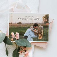 Folded wedding greeting card featuring romantic couple portrait with “And they lived happily ever after” text, styled with blush envelope and greenery.
