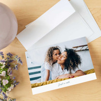 Folded photo card with a mother and child image and “Just a note” text, shown with envelope and flowers.