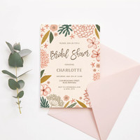 Flat bridal shower invitation card with illustrated floral border, event details, and matching blush envelope, styled with greenery on neutral background.