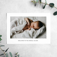 Landscape flat birth announcement card featuring sleeping newborn photo and welcome message, styled on light textured surface with greenery.