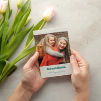 Flat photo card featuring a grandmother and child hugging, with “Grandma, A Legacy of Love” text, held in hands beside tulips.