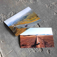 Two travel-themed landscape prints on a stone surface, one showing a mountain road and the other a straight desert path
