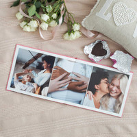 Open layflat photo book with three images of a couple relaxing and embracing, surrounded by white roses, chocolates, and ribbon
