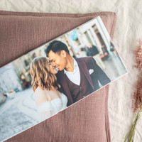 Layflat photo book displaying a full-bleed wedding portrait of a couple embracing on a city street, resting on textured fabric with dried florals.