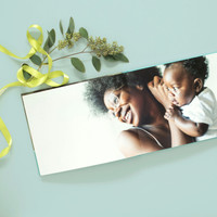 Open layflat photo book featuring a smiling mother holding her baby, styled with ribbon and greenery.