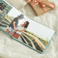 Layflat photo book showing a mother and daughter walking together along a wooden beach path, styled with a wrapped gift.
