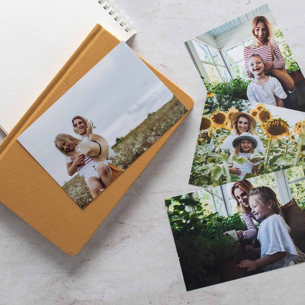A collection of printed photos showing a woman and child outdoors and gardening, arranged on a white surface with a mustard yellow journal