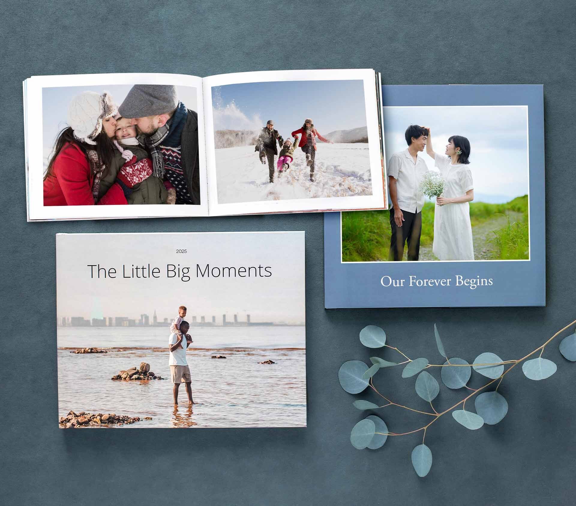 An assortment of custom photo books displayed on a dark surface, with one opened to winter photos and the others featuring wedding and family themes