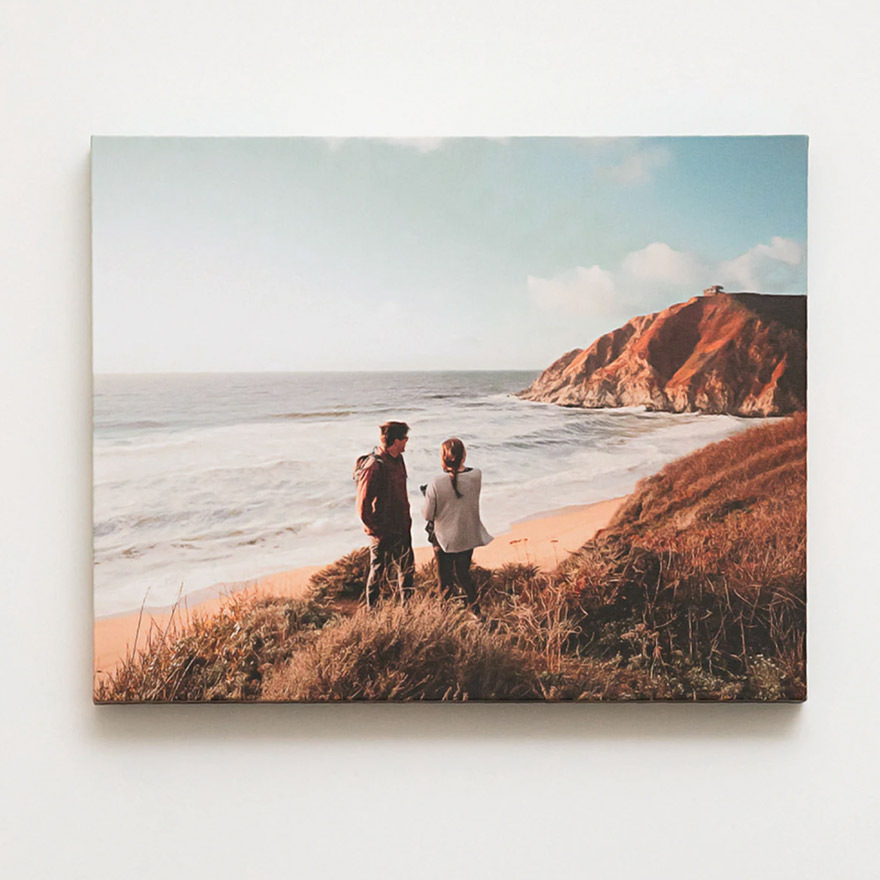 Canvas print of a couple standing on a coastal cliffside path overlooking the ocean, with golden grass and rugged shoreline in view