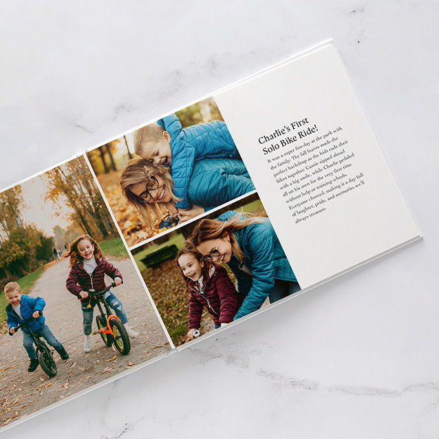 Layflat photo book open to a fall-themed spread with children riding a bike and a mother helping them