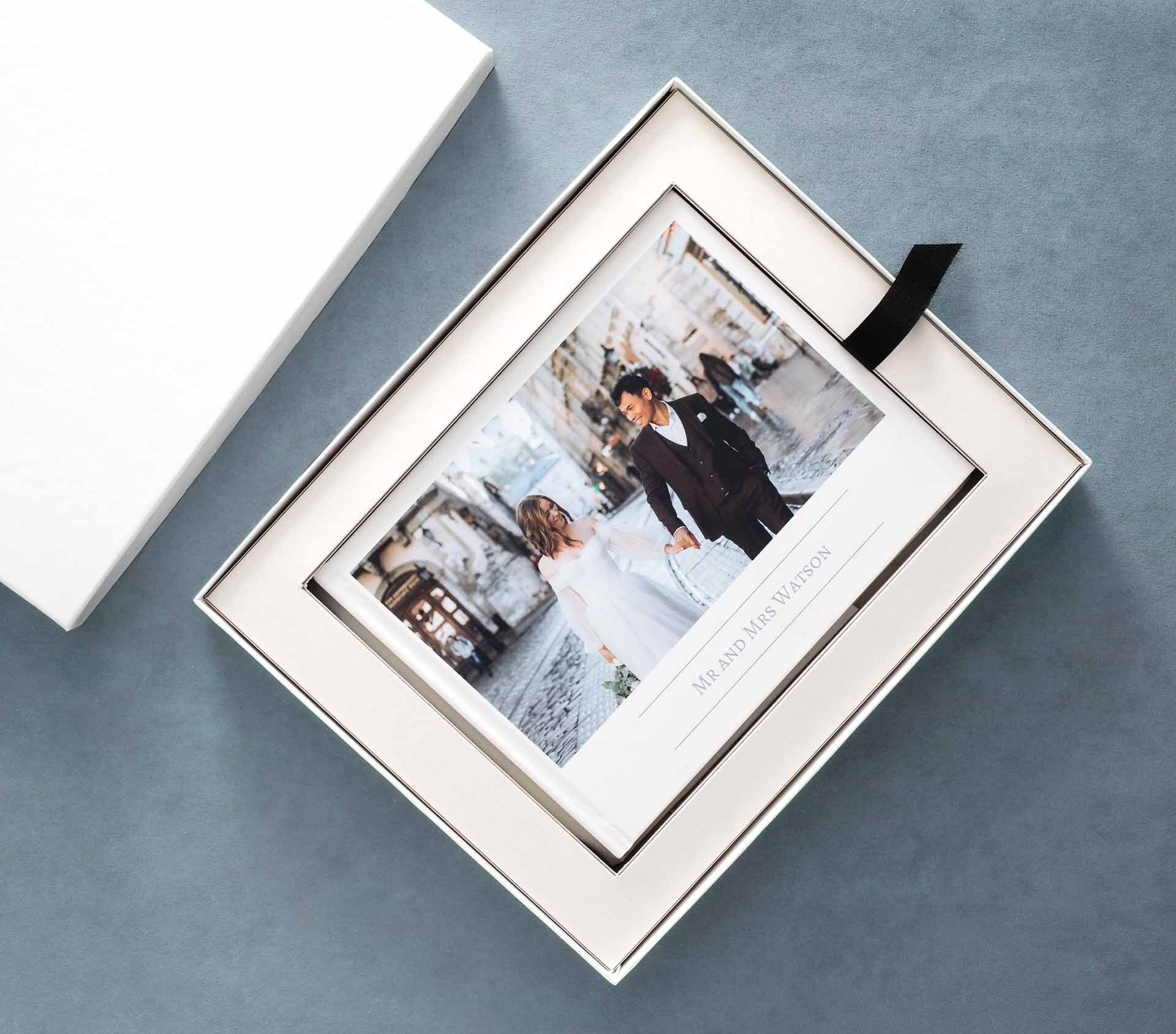 Layflat photo book with a wedding photo on the cover, placed inside an elegant white presentation box