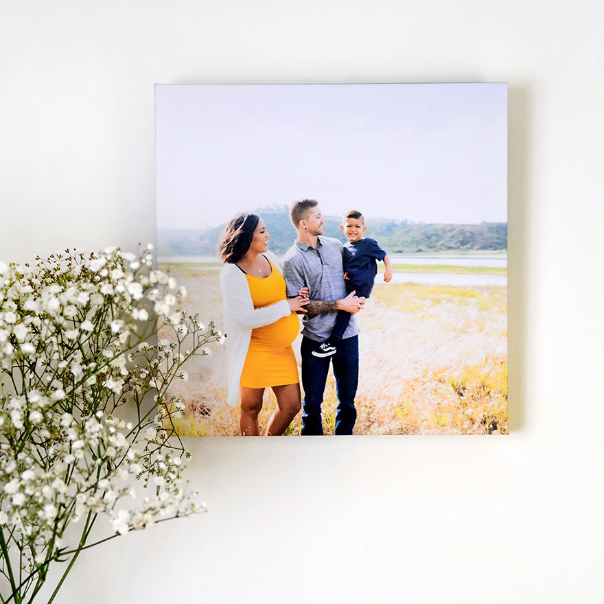 Canvas wall decor displaying a family walking in a grassy field with a child, mounted on a light wall beside small white flowers.