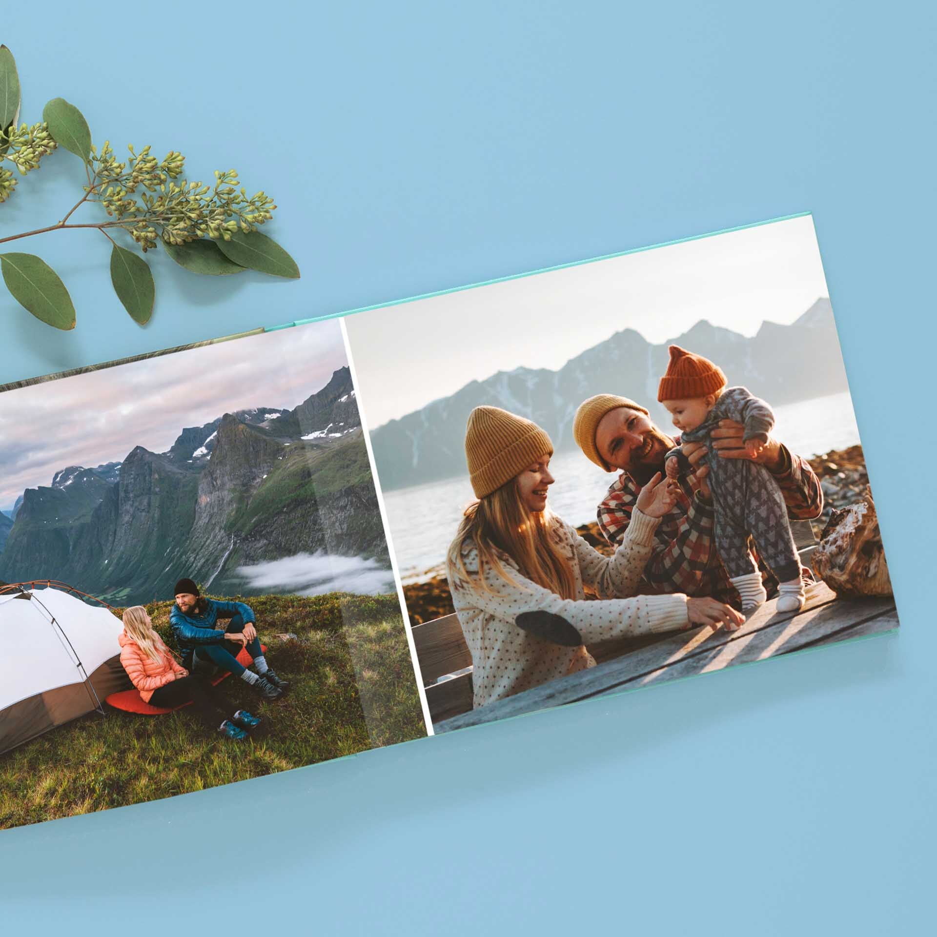 Layflat photo book spread with family mountain camping photo on left and family portrait on right, displayed on blue background.