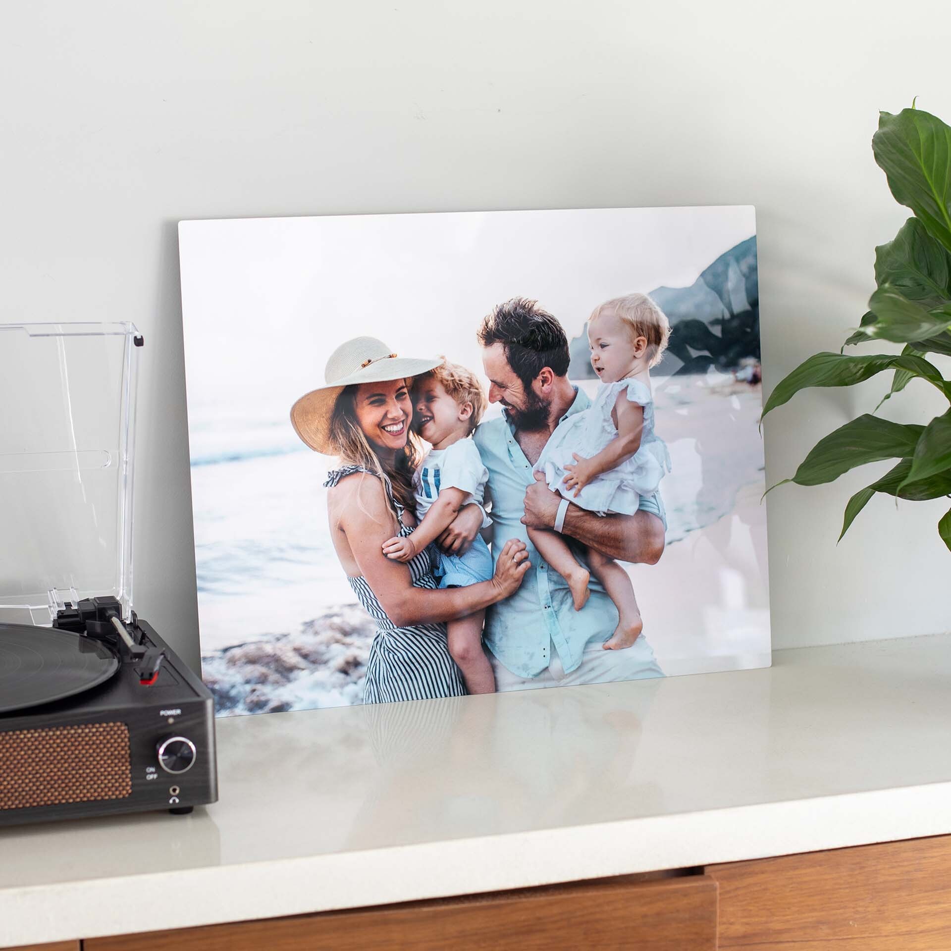 Custom metal wall decor featuring a family beach portrait, displayed on a light-colored console table beside a record player and potted plant.