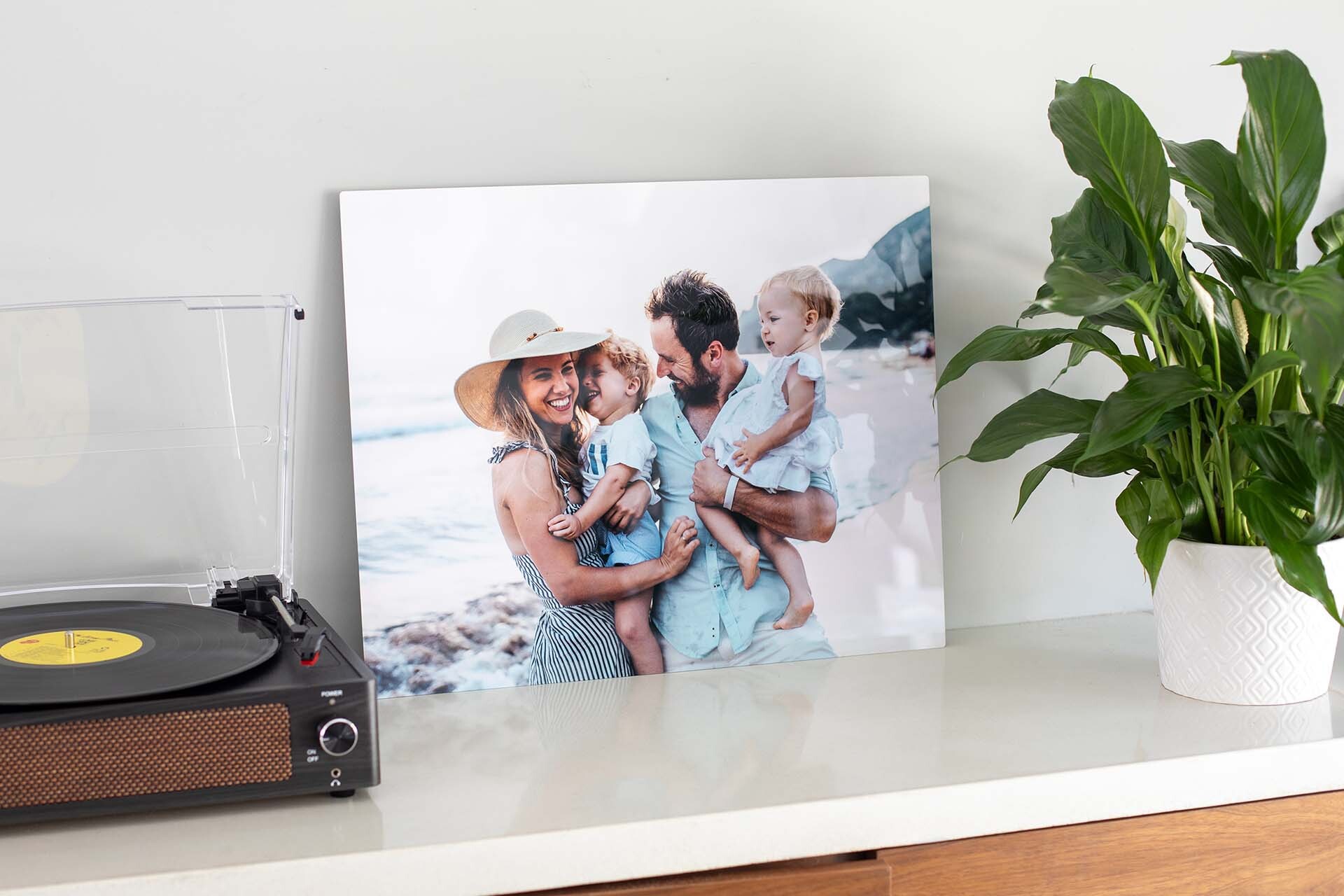 Custom metal wall decor featuring a family beach portrait, displayed on a light-colored console table beside a record player and potted plant.